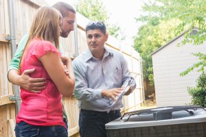 Technician explaining AC maintenance to a couple next to an outdoor unit.