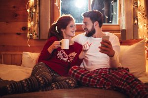Happy couple relaxing in cozy, warm room with winter clothes and hot drinks, enjoying reliable home heating.