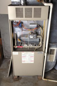 Open gas furnace unit showing internal components during furnace installation in a residential garage. 