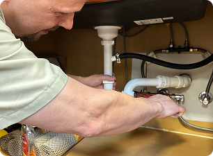 plumber working on pipes underneath a sink